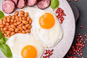 English breakfast with fried eggs, bacon, beans, tomatoes, spices and herbs photo