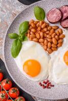 English breakfast with fried eggs, bacon, beans, tomatoes, spices and herbs photo