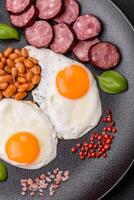 English breakfast with fried eggs, bacon, beans, tomatoes, spices and herbs photo
