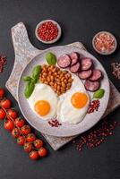 English breakfast with fried eggs, bacon, beans, tomatoes, spices and herbs photo