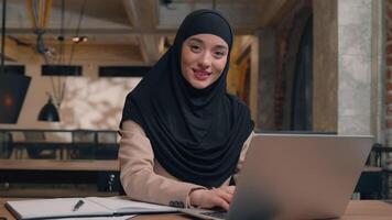 Happy friendly girl Muslim islamic woman in hijab student working laptop at cafe office female Arabian businesswoman business employer lady cheerful smile invite come here welcome gesture invitation video