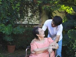 Happy Asian senior woman sitting on wheelchair with her son in the garden. talking , looking to each other. photo