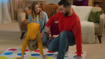 Caucasian happy family playing funny game twister at home weekend children play with parents active carefree mother father kids little girls daughters have fun laughing entertainment childhood custody video