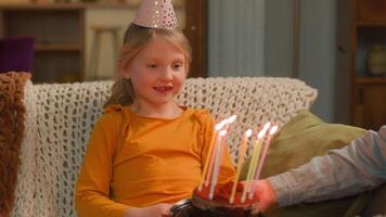 caucásico pequeño niña sonriente niño niño hija Chica de escuela hembra bebé en festivo gorra contento cumpleaños celebracion soplo velas en festivo pastel deseo sorpresa madre felicitar niños nacimiento fiesta video