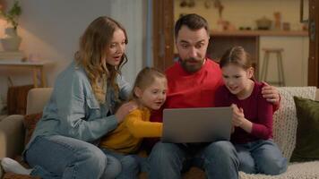 gelukkig opgewonden Kaukasisch familie winnaars mam vader weinig kinderen meisjes dochters kinderen broers en zussen vieren prestatie boodschappen doen laptop winnen inzet verheugen schok verrassing mooi zo nieuws Aan huis bankstel sofa samen video