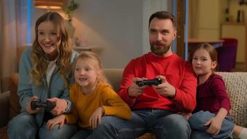 Caucasian family mom dad playing online cyber game home weekend fun gaming addiction happy joyful children kids little girls daughters and parents play console joysticks celebrate win hive five video