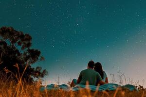 Pareja estudio de las estrellas en cobija en prado, contando disparo estrellas en claro verano noche foto