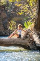 niña sentado en un grande árbol encima el río foto