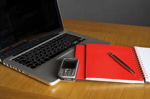 teléfono, computadora portátil y cuaderno vacío en el escritorio foto