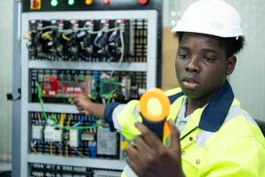 retrato de un técnico trabajando con un digital multímetro a prueba el eléctrico sistema de un enorme circuito tablero a un industrial planta utilizando un automatizado mano robot. foto