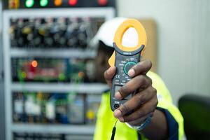 retrato de un técnico trabajando con un digital multímetro a prueba el eléctrico sistema de un enorme circuito tablero a un industrial planta utilizando un automatizado mano robot. foto