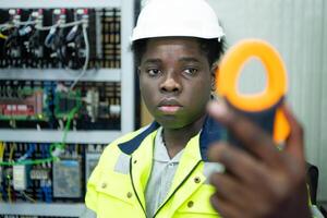 Portrait of a technician working with a digital multimeter to test the electrical system of a huge circuit board at an industrial plant using an automated hand robot. photo