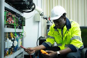 Portrait of a technician working with a digital multimeter to test the electrical system of a huge circuit board at an industrial plant using an automated hand robot. photo