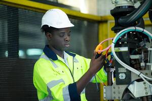 retrato de un técnico trabajando con un digital multímetro a prueba el eléctrico sistema de un enorme circuito tablero a un industrial planta utilizando un automatizado mano robot. foto