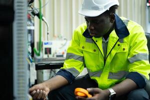 Portrait of a technician working with a digital multimeter to test the electrical system of a huge circuit board at an industrial plant using an automated hand robot. photo