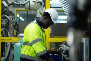 retrato de un técnico trabajando con un digital multímetro a prueba el eléctrico sistema de un enorme circuito tablero a un industrial planta utilizando un automatizado mano robot. foto