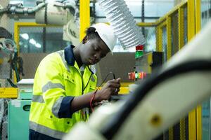 Portrait of a technician working with a digital multimeter to test the electrical system of a huge circuit board at an industrial plant using an automated hand robot. photo