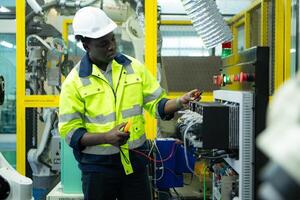 Portrait of a technician working with a digital multimeter to test the electrical system of a huge circuit board at an industrial plant using an automated hand robot. photo