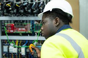 retrato de un técnico trabajando con un digital multímetro a prueba el eléctrico sistema de un enorme circuito tablero a un industrial planta utilizando un automatizado mano robot. foto