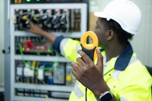 retrato de un técnico trabajando con un digital multímetro a prueba el eléctrico sistema de un enorme circuito tablero a un industrial planta utilizando un automatizado mano robot. foto