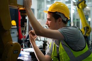 Technician who maintains a small robot arm the operation of a small robot arm used in industry is being repaired. photo