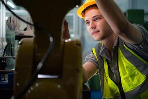 Technician who maintains a small robot arm the operation of a small robot arm used in industry is being repaired. photo