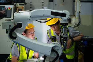 Technician who maintains a small robot arm the operation of a small robot arm used in industry is being repaired. photo