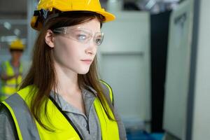 Portrait of a female factory worker wearing a hard hat looking at a computer screen used to control production. photo