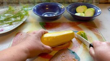 Female hands cutting yellow zucchini on a glass wooden board, close-up video