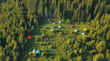 voar sobre uma barraca acampamento grupo do turistas dentro a montanhas às nascer do sol. batata Cidade do uma grupo do alpinistas a partir de uma pássaro olho visualizar. turista acampamento dentro a verde floresta video