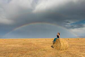 hermosa joven niña en un campo con Paja en un antecedentes de arco iris foto