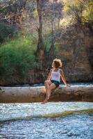 contento joven mujer posando en un Iniciar sesión terminado un río foto