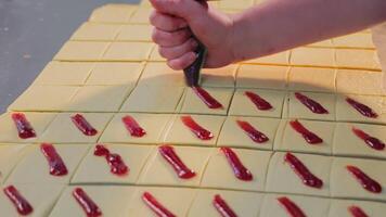 A chef uses a pastry bag to squeeze raspberry filling onto a piece of dough, close-up. Cookie baking concept video