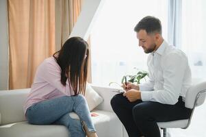 Beautiful girl telling to psychotherapist about her troubles, doctor writing down some notes. Female patient explaining purpose of a visit to psychologist while doctor filling in her medical card photo