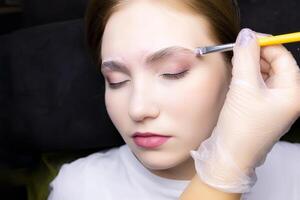 the blonde model is lying on a black couch with a white T-shirt, she is undergoing the procedure of lamination of eyebrows and photo