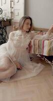 Young fashionable model wearing vintage bridal dress sitting on floor, posing at home in stylish vintage interior video