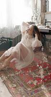 Young fashionable model wearing vintage bridal dress sitting on floor, posing at home in stylish vintage interior video