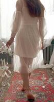 Legs of fashionable woman wearing vintage wedding dress posing at home and holding in hands flowering branch video