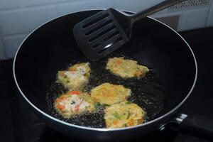 Someone is turning a dough of raw vegetables and wheat flour which is fried photo