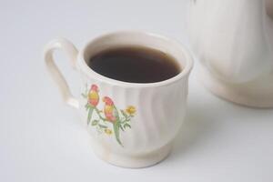 cerca arriba foto de un taza de dulce té y un blanco tetera con cerámico material