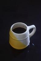 Black coffee in a white and yellow cup on a black ceramic table photo