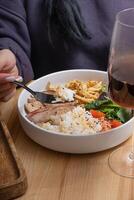 A woman's hand holds a fork with rice, veal and vegetables in bowl. The concept of a balanced diet photo