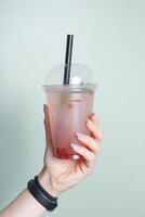 Plastic glass with bubble tea and ice in female hand. Trendy cold summer drink photo