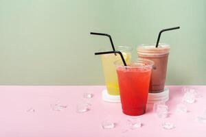 Three takeaway glasses of summer drinks with ice. Lemonade on coloured background photo