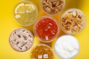 Takeaway glasses of summer drinks with ice top view. Lemonades and coctails on yellow background photo