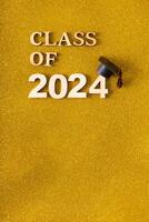 Class of 2024 text with graduated cap on golden glitter background. Graduation holiday concept. photo