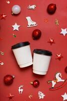 Mockup of cardboard coffee cups with Christmas decorations flat lay, top view on red background. photo