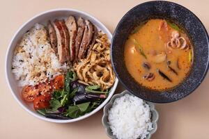 Bowl with rice, veal and vegetables and tom yam soup with seafood top view photo