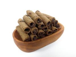 Chocolate wafers rolled in a wooden bowl isolated on white background. A delicious snack that tastes sweet and crunchy photo