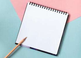 Mock up of empty spiral sketchbook with white paper on pastel pink and blue background. Top view of open notebook with clean sheet. Template for message. Copy space. photo